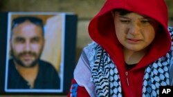FILE - During a protest in Beirut, Lebanon, on Dec. 8, 2023, a boy weeps as he sits next to a portrait of Reuters visuals reporter Issam Abdallah, who was killed when an Israeli shell landed in a gathering of international journalists on Oct. 13, 2023.