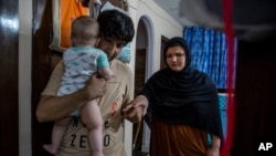 Mohammad Nabi holds his seven-month-old daughter Bahar as he helps his wife, a former Afghan policewoman Khatera Hashmi inside a rented accommodation in New Delhi, India, on Aug. 13, 2021.
