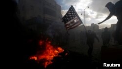 A Palestinian protester prepares to burn a U.S. flag during clashes with Israeli troops at a protest against U.S. President Donald Trump's decision to recognize Jerusalem as the capital of Israel, near the Jewish settlement of Beit El, near the West Bank 