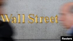 FILE - People walk by a Wall Street sign close to the New York Stock Exchange in New York.
