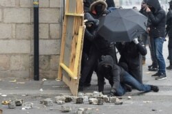 Protesters hide behind a wooden board and an umbrella during a demonstration against the pension overhauls, in Nantes, Dec. 5, 2019, as part of a national general strike.