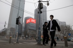 Residents walk past a retail and office district with a screen showing propaganda which reads "Go China! Go Wuhan" as businesses slowly restart in Beijing, March 8, 2020.