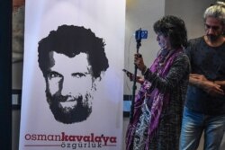 FILE - A journalist stands in front of a poster featuring jailed philanthropist Osman Kavala, during a press conference given by his lawyers, in Istanbul, Turkey, Oct. 31, 2018.