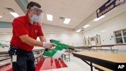 Wearing masks and face guards as protection against the spread of COVID-19, Garland Independent School District custodian Raul Vela mists surfaces for cleaning in the cafeteria at Stephens Elementary School in Rowlett, Texas, July 22, 2020.