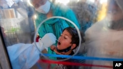 A health worker takes a swab from a Kashmiri boy to test for COVID-19 in Srinagar, Indian-controlled Kashmir, May 8, 2021. Infections have swelled in India since February; more contagious variants and permissive decisions on gatherings are blamed.