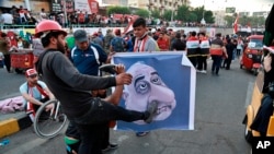 Protesters hit a poster showing Iraqi Prime Minister Adel Abdel-Mahdi with shoes during ongoing anti-government protests in Baghdad, Iraq, Nov. 3, 2019. 