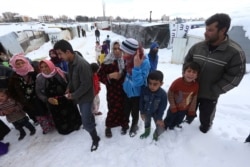 Syrian refugees wait to receive plastic cover for their tents at a refugee camp in Zahleh, Bekaa Valley, Lebanon, Jan. 8, 2015.