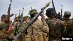 FILE - Iraqi Shi'ite paramilitary personnel carry their weapons as they gather on the outskirts of Baiji, June 3, 2015.