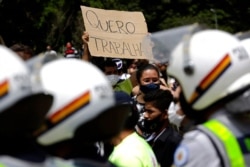 A demonstrator holds up the Portuguese message "I want to work" outside a city government office where police stand guard during a protest against a two-week-long lockdown to curb the spread of COVID-19 in Brasilia, Brazil, March 1, 2021.