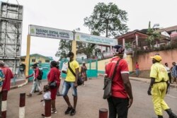 FILE - People wear masks to protect against the COVID-19 coronavirus as they walk by the entrance to the Yaounde General Hospital in Yaounde, March 6, 2020.