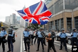 FILE - A woman waves a British flag as policemen in anti-riot gear stand guard against protesters on a closed-off road near the Legislative Council in Hong Kong, June 12, 2019.