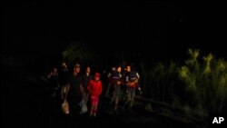 Un grupo de personas con hijos en sus brazos llega a un centro de procesamiento de migrantes que quieren asilarse en EE.UU., el 12 de mayo del 2021 en La Joya, Texas. 