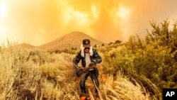 David Garfield clears a fire break around his home as the Sugar Fire, part of the Beckwourth Complex Fire, burns toward Doyle, Calif., July 10, 2021.