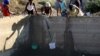 Women use buckets and cloth to collect stagnant rain water from an unfinished sewerage treatment tank, now used as a well, to do their laundry in Senekal, South Africa where taps and water sources have run dry, Jan. 7, 2016.