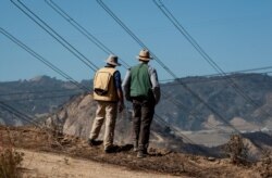 FILE - Fire investigators examine the scene around a transformer tower in Sylmar, Calif., suspected of being responsible for starting the Saddleridge fire, Oct. 15, 2019.
