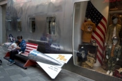 FILE - A woman tends to a child near a promotional gimmick in the form of a bomb and the U.S. flag outside a U.S. apparel shop in Beijing.