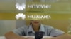 A sales assistant looks at her mobile phone as she waits for customers behind a counter at a Huawei booth in Wuhan, Hubei province, China.