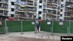 FILE - A man wearing a face mask keeps watch at an entrance to a residential community that has been fenced in with temporary barriers, in Yichang city of Hubei, the province hit hardest by the novel coronavirus outbreak, Feb. 10, 2020.