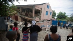Residents stand looking at a collapsed school damaged bya magnitude 5.9 earthquake the night before, in Gros Morne, Haiti, Oct. 7, 2018. 