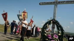 A religious procession passes an Orthodox cross with a sign reading Save and Guard at the crash site of the Malaysia Airlines Flight 17, near the village of Hrabove, eastern Ukraine, July 17, 2015. 
