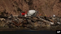 A cement truck and workers are seen from the water among beachfront homes destroyed by the Palisades Fire, Jan. 15, 2025, in Malibu, California.
