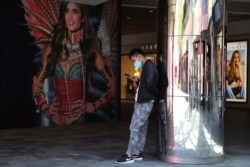 FILE - A man wearing Nike shoes uses his smartphone near an advertisement for U.S. lingerie maker Victoria's Secret, in Beijing, China, May 21, 2019.