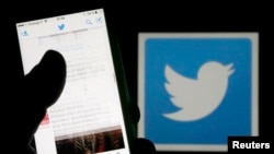 FILE - A man reads tweets on his phone in front of a displayed Twitter logo in Bordeaux, southwestern France, March 10, 2016. 