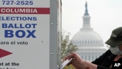 FILE - With the U.S. Capitol dome visible, a voter drops a ballot into an early voting drop box, Oct. 28, 2020, at Union Market in Washington. 