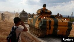 FILE - A boy salutes as Turkish Armed Forces vehicles drive pass by a village on the Turkish-Syrian border line in Reyhanli, Hatay province, Turkey, Oct. 11, 2017. 