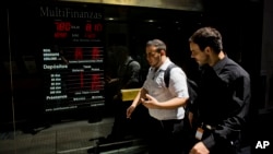 People walk by a sign indicating the exchange rate between the Argentine peso and the U.S. dollar in Buenos Aires, Jan. 23, 2014. 