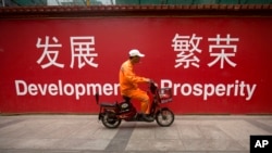 资料照：一名男子骑车路过北京市中心一堵宣传墙。（2015年7月15日）