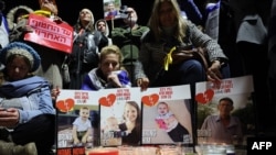 Orang-orang berkumpul di balik poster empat sandera Israel, beberapa jam setelah empat jenazah diserahkan ke Israel oleh kelompok Hamas Palestina, dalam acara doa bersama untuk menghormati mereka di lapangan penyanderaan di Tel Aviv pada 20 Februari 2025. (Foto: Jack Guez/AFP)