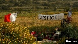 Una manta pidiendo justicia es vista junto a la foto de la asesinada periodista anticorrupción, Daphne Caruana Galizia, en el lugar donde explotó la bomba que la mató en Malta en abril del 2018.