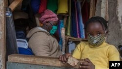 FILE - A fabrics trader and her child wear face masks to guard against the new coronavirus inside her shop in Lilongwe, Malawi, May 18, 2020. 