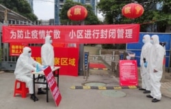 FILE - Workers in protective suits are seen at a checkpoint for registration and body temperature measurement, at an entrance to a residential compound in Wuhan, Hubei province, China, Feb. 13, 2020.