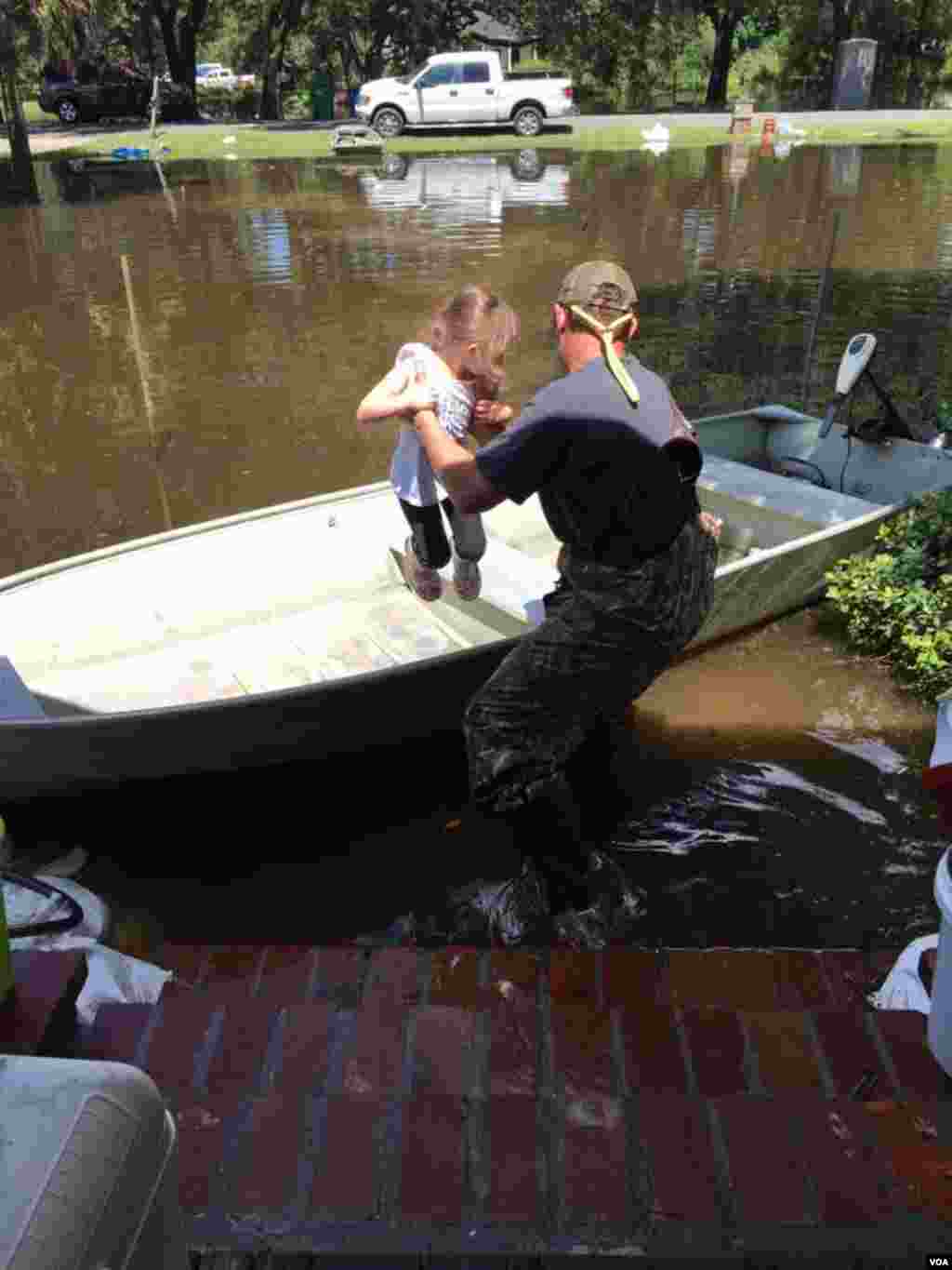 Graham Kinchen di St. Amant, Louisiana membawa anaknya naik perahu di depan rumah mereka. (VOA/M. Melton)