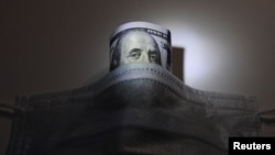 Selembar uang kertas dollar AS di balik masker untuk melindungi dari virus corona (Covid-19), dalam foto ilustrasi pada 18 Maret 2020. (Foto: Reuters)
