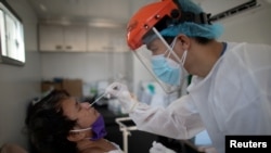 FILE - A nurse gets a swab from a man under observation for coronavirus disease (COVID-19) in a booth set up in a hospital parking lot in Manila, Philippines, April 15, 2020. 
