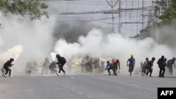Protesters run from tear gas fired by security forces, as some demonstrators also let off fire extinguishers, next to a barricade set up during the demonstration against the military coup in Mandalay, March 15, 2021.