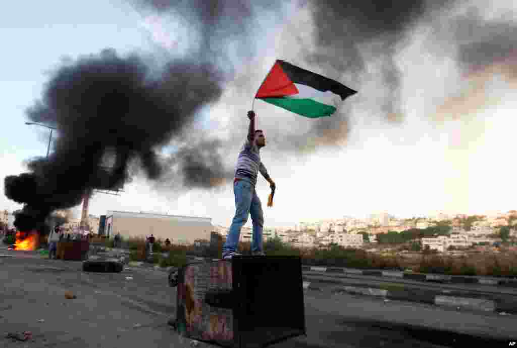 A Palestinian man waves the national flag during a protest against Israel's operations in Gaza Strip, outside Ofer, an Israeli military prison near the city of Ramallah, November 18, 2012.