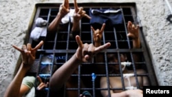 FILE - People arrested for being members of MS-13 (the Mara Salvatrucha street gang), among other crimes, flash their gang's hand sign from inside a jail cell at a police station in San Salvador, Oct.12, 2012.