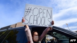 Miembros de la Coalición de Estudiantes Primero de Los Ángeles exhiben carteles que piden la reapertura de las escuelas en vehículos que pasan durante un mitin, el 15 de febrero de 2021.