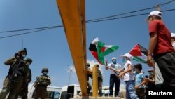 Demonstrators hold Palestinian flags in front of Israeli soldiers during a protest against the United Arab Emirates' deal with Israel to normalize relations, in Haris near Salfit in the Israeli-occupied West Bank, Aug. 14, 2020.