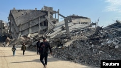 গাজায় ধ্বংস হয়ে যাওয়া বাড়ি ও দালানের ধ্বংসাবশেষের মধ্য দিয়ে হেঁটে যাচ্ছেন ফিলিস্তিনিরা। 