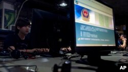 FILE - Computer users sit near a monitor display with a message from the Chinese police on the proper use of the Internet at an Internet cafe in Beijing, China.