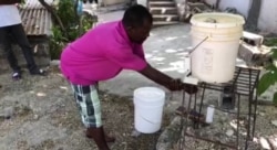 Adults and children alike come to wash their hands at the hands-free bucket in teen Wens Dimanche's backyard. (Photo: Matiado Vilme / VOA)