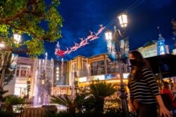 FILE - A shopper wearing a face mask walks by the Christmas decorations at The Grove outdoor shopping center, amid the Coronavirus pandemic, Nov. 5, 2020, in Los Angeles.