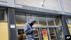 A pedestrian wears a face mask while standing outside the High School of Economics & Finance closed due to coronavirus concerns, Monday, March 16, 2020, in New York. 