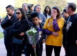 A Kobe Bryant fan brings flowers as other admirers grieve at a small memorial at the entrance of the Mamba Sports Academy in Thousand Oaks, Calif., Jan. 26, 2020.