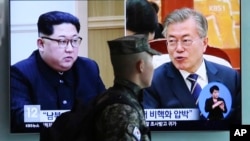 A South Korean marine passes by a TV screen showing file footage of South Korean President Moon Jae-in and North Korean leader Kim Jong Un, left, during a news program at the Seoul Railway Station in Seoul, South Korea, April 18, 2018.